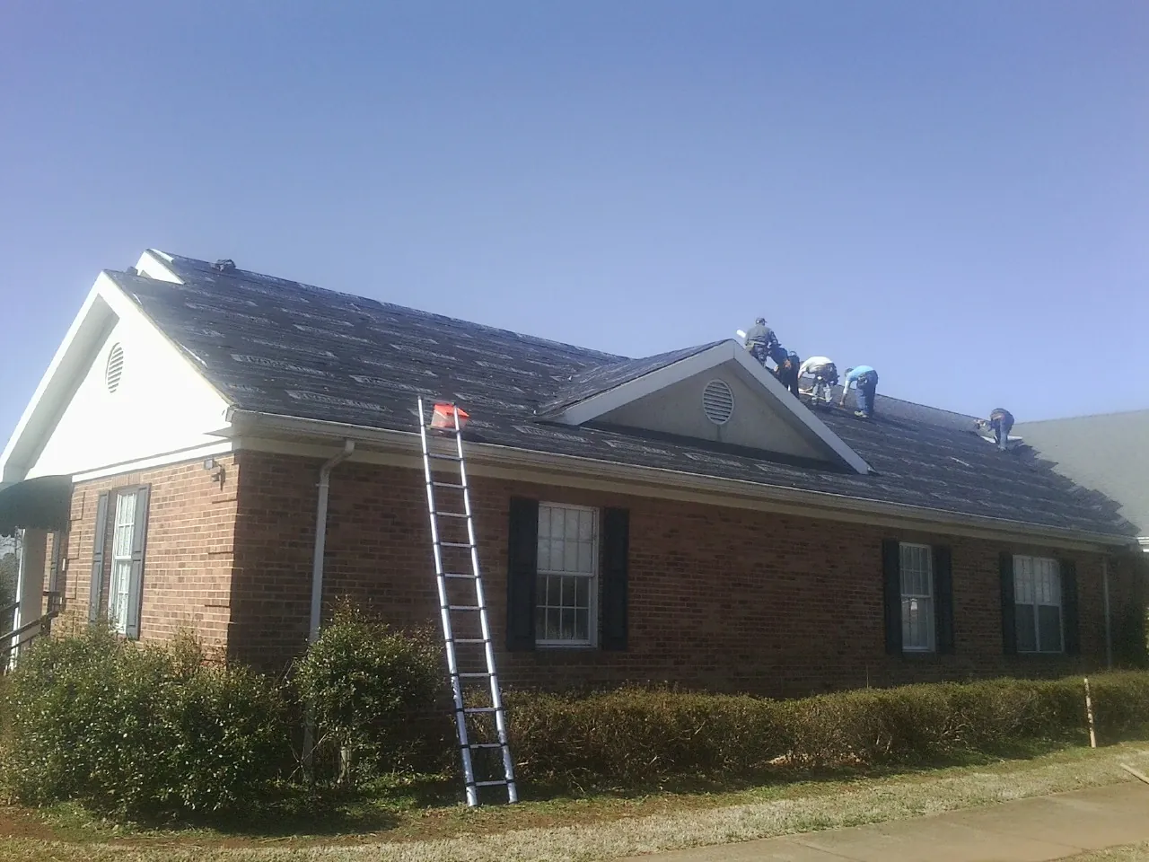 Crew tearing shingles off a brick ranch roof with a ladder set — Emergency Roof Repair work by our crew in Ripley