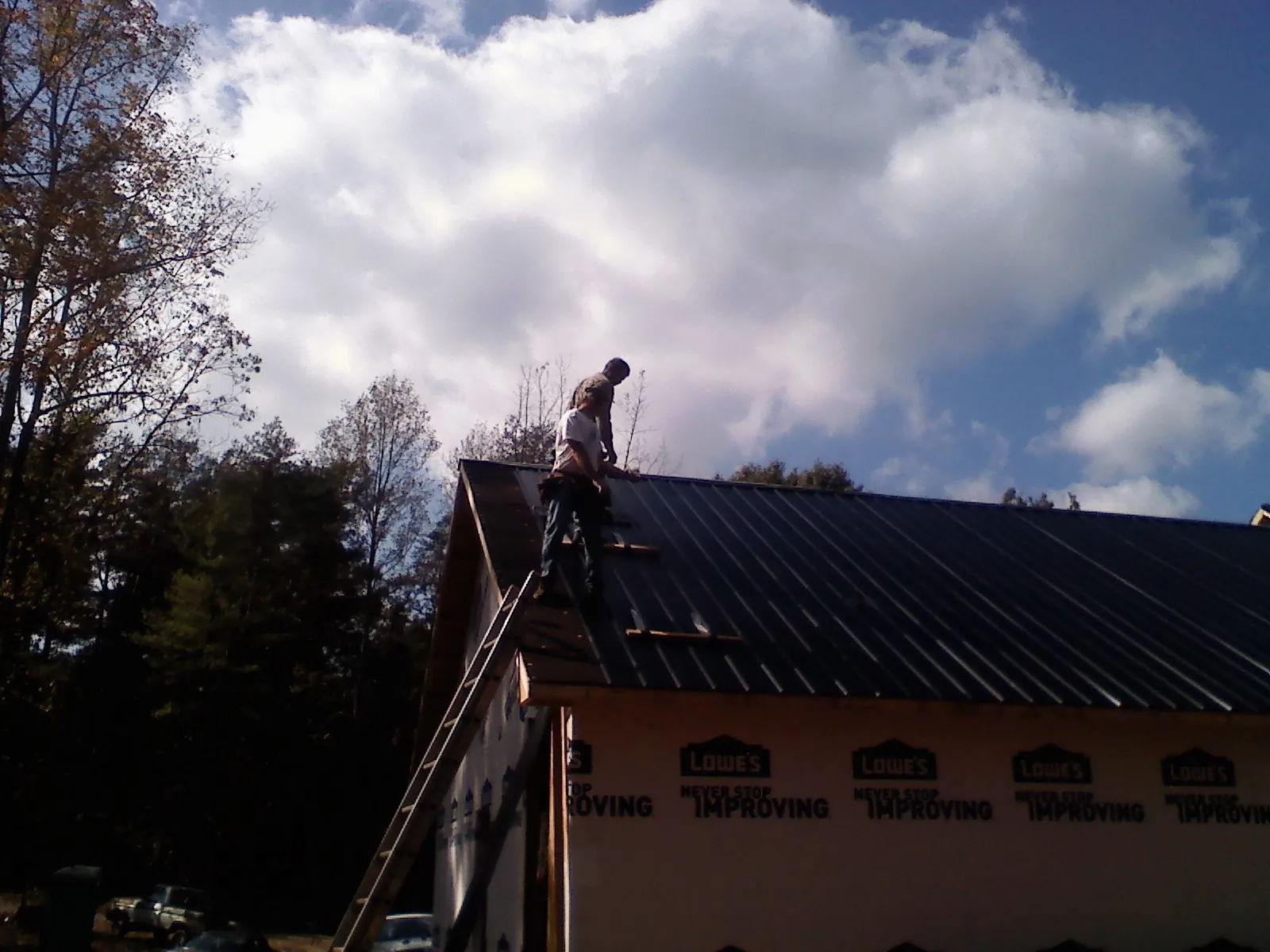 Roofer fastening dark metal panels high against a cloudy sky, from a Roof Inspection job in Ripley